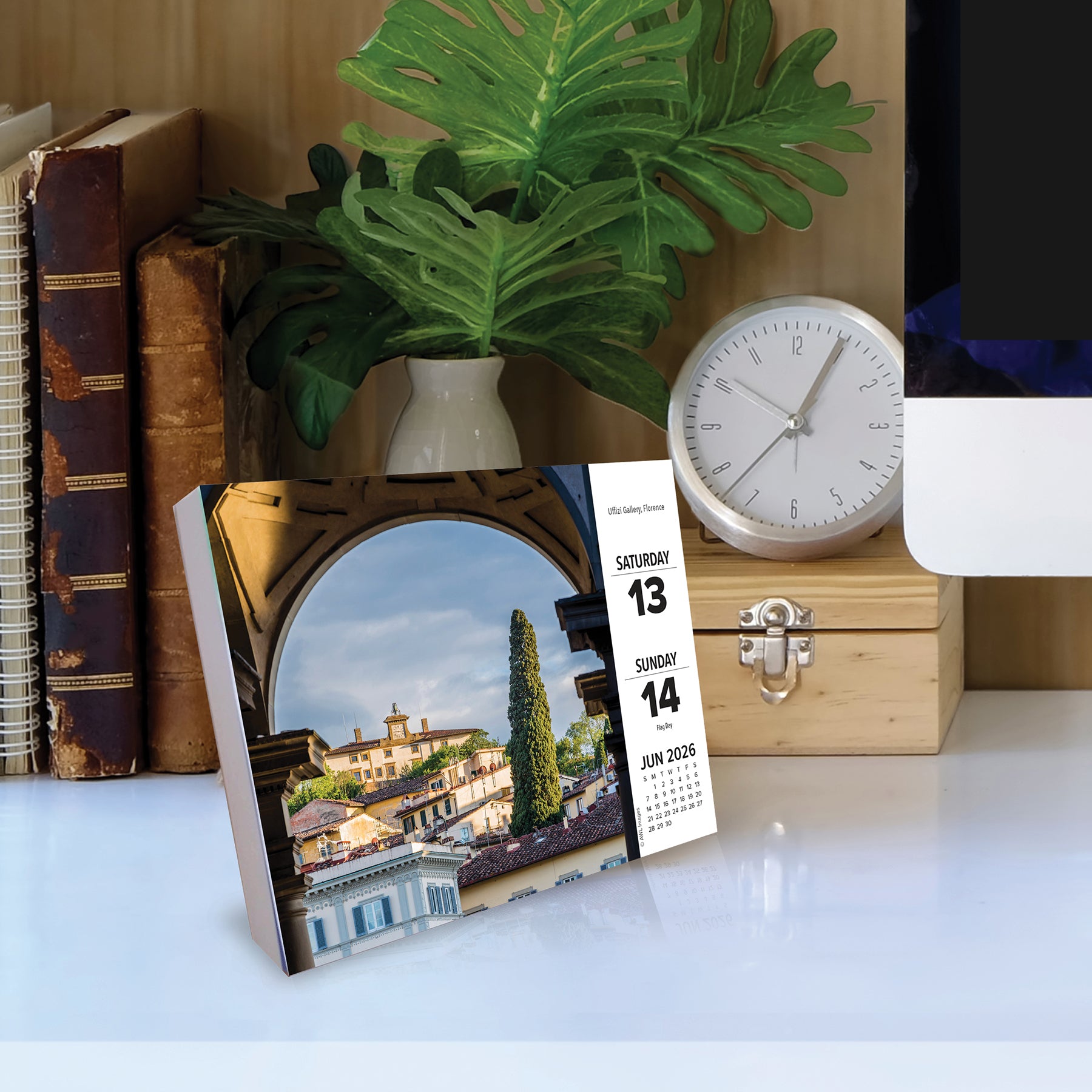2026 Daily Box Calendar displayed on a desk with an Italian landscape image and a clock in the background.