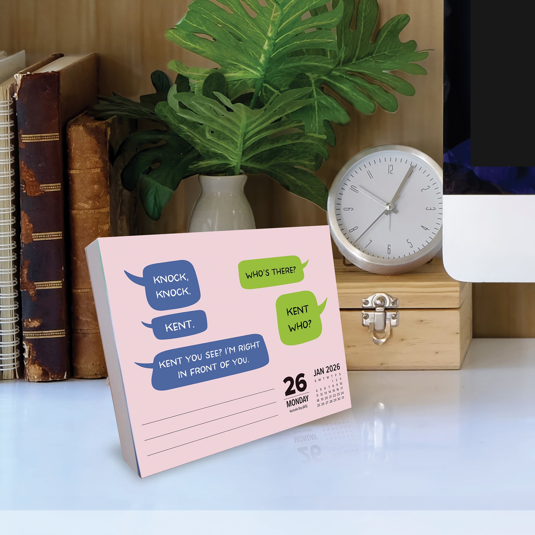 2026 Daily Box Calendar featuring knock-knock jokes on a desk with a plant and clock.
