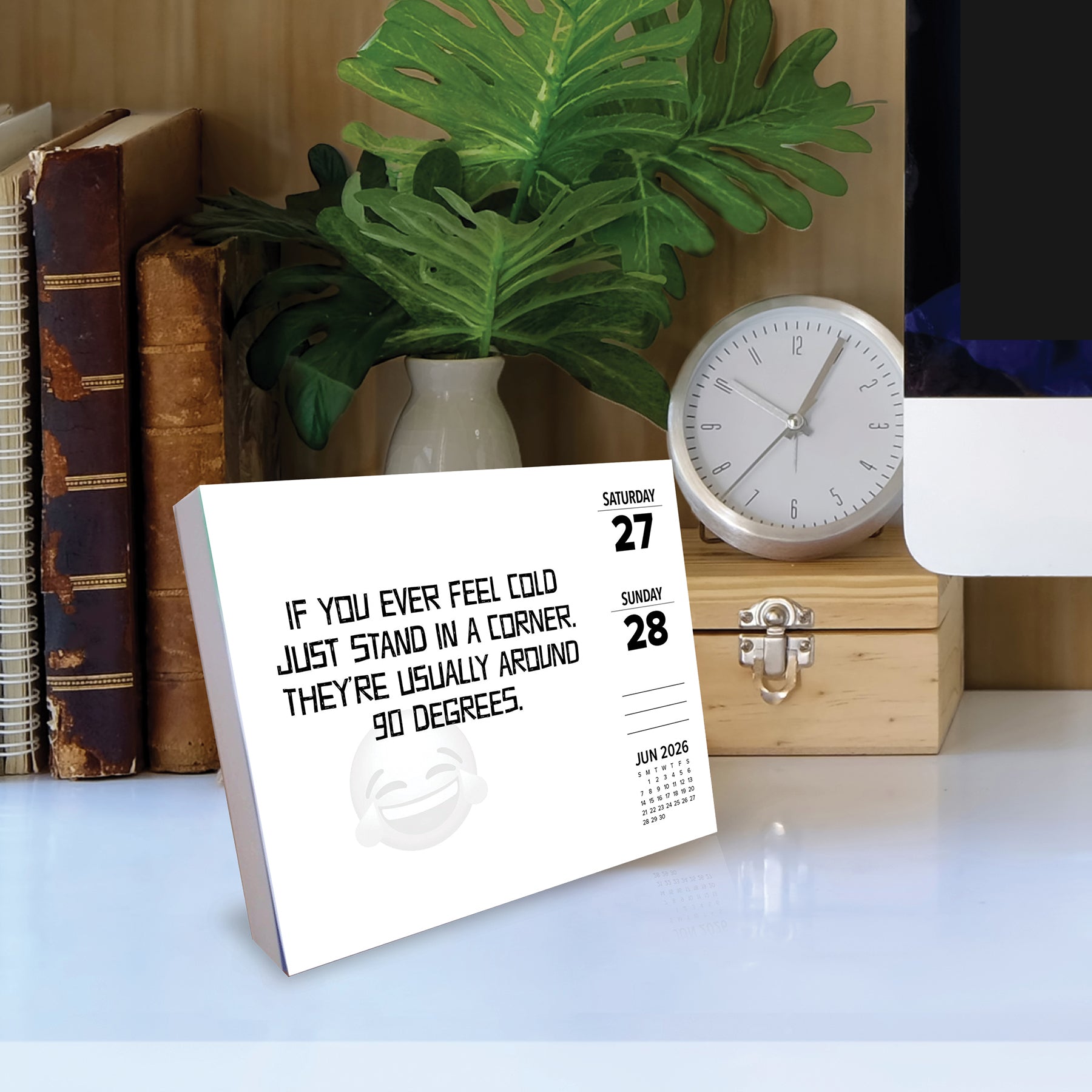 2026 Daily Box Calendar featuring a punny joke on a desk with a clock and plant.