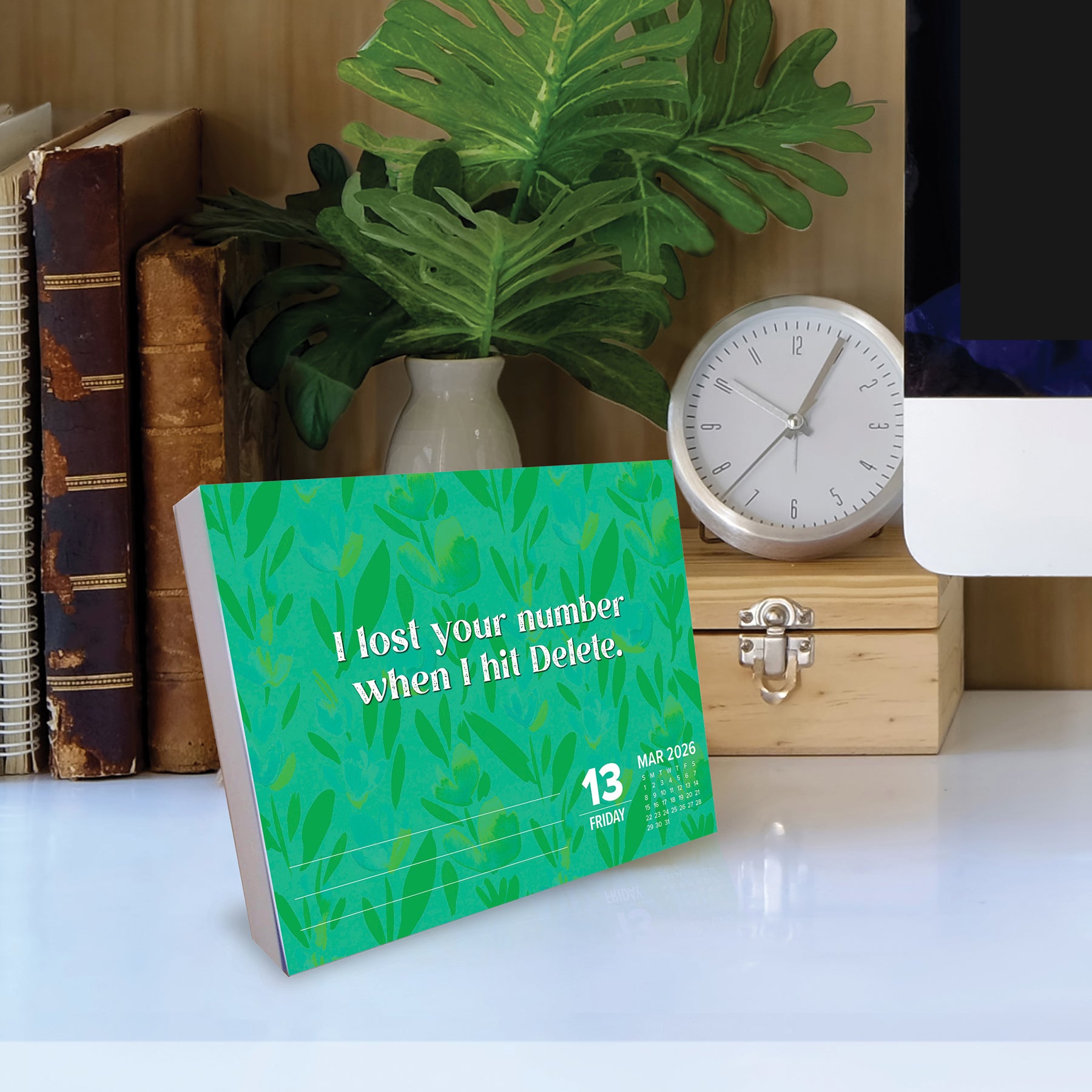 Make Every Day Your Bitch 2026 Daily Box Calendar on desk with quote about losing numbers, surrounded by books and plants.