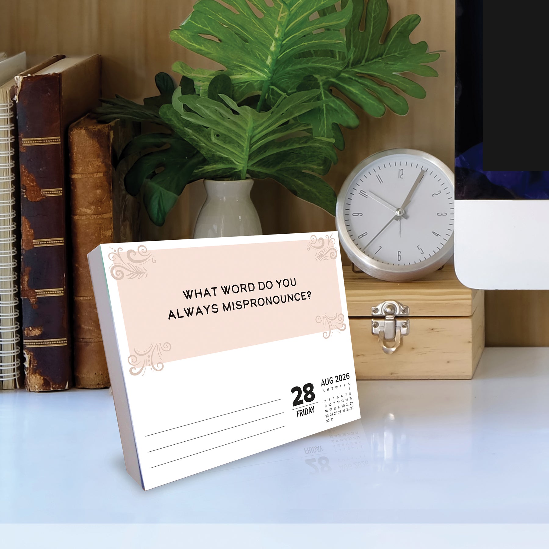 2026 Daily Box Calendar with a question about mispronunciation on a desk with books and a clock.