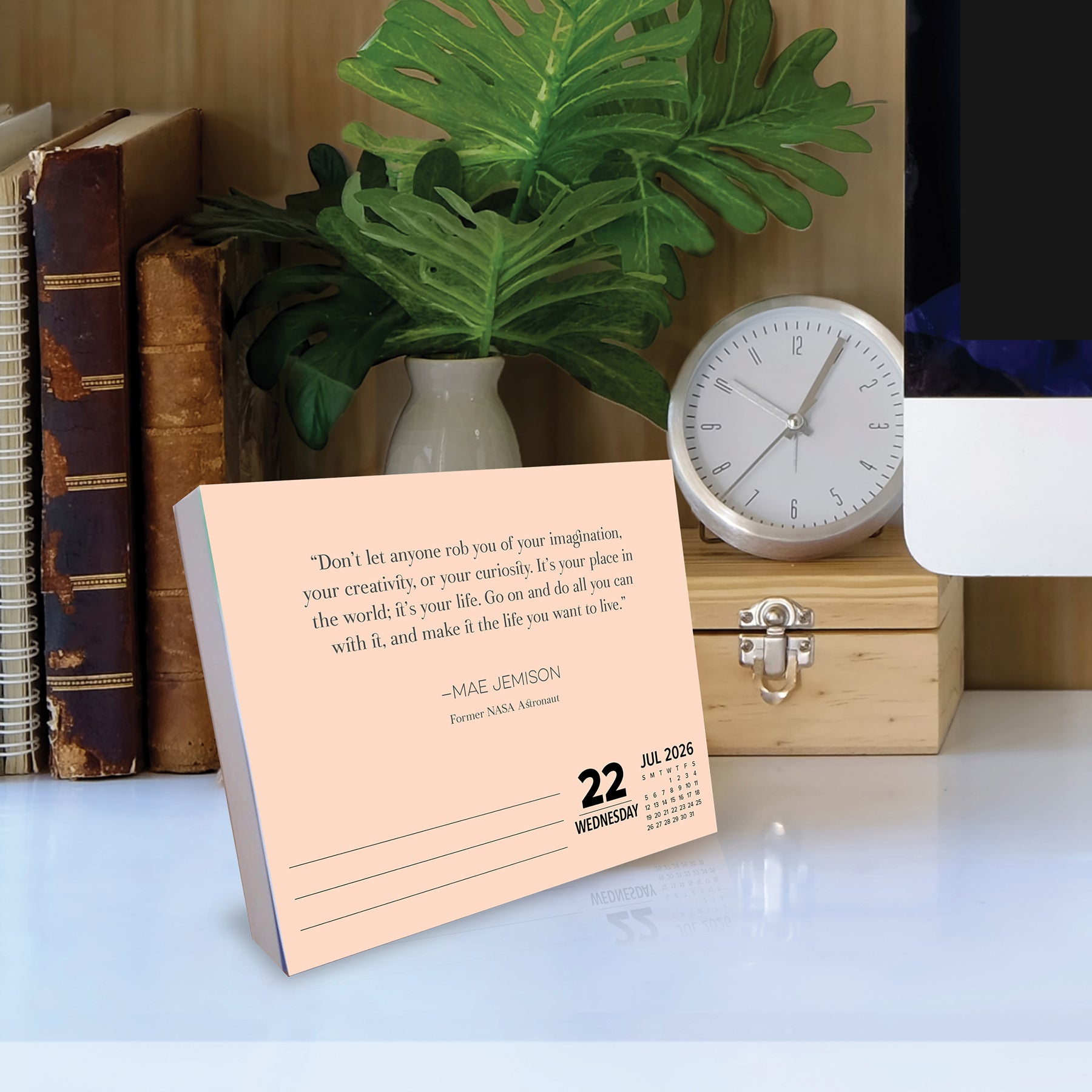 2026 Daily Box Calendar displayed on a desk with a quote by Mae Jemison, surrounded by plants and books.