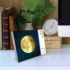 Moon Magic 2026 Daily Box Calendar displaying a golden moon illustration on a dark background in a cozy workspace.