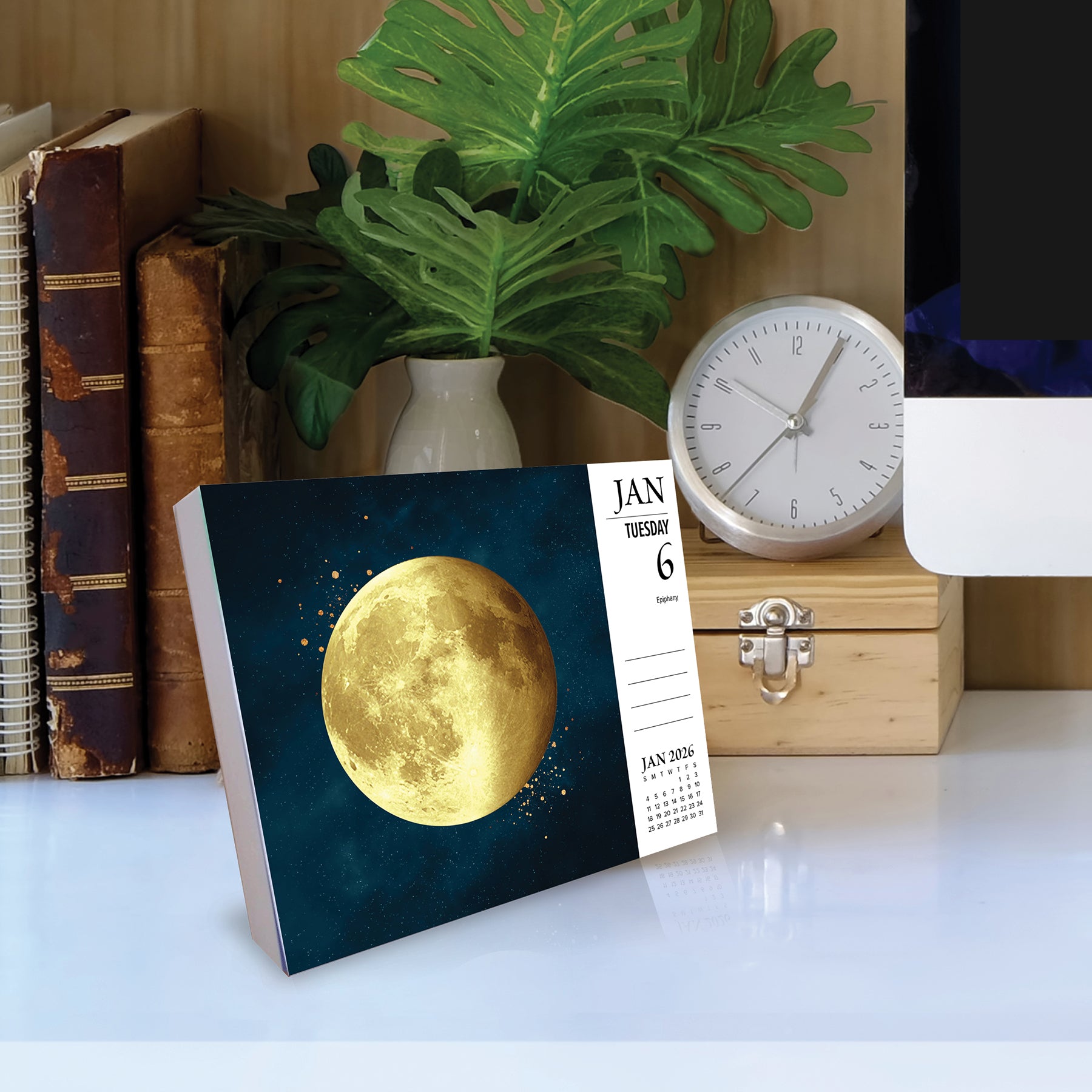 Moon Magic 2026 Daily Box Calendar displaying a golden moon illustration on a dark background in a cozy workspace.